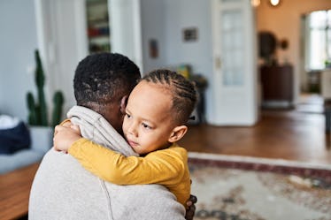 A Black child hugging their father at home.