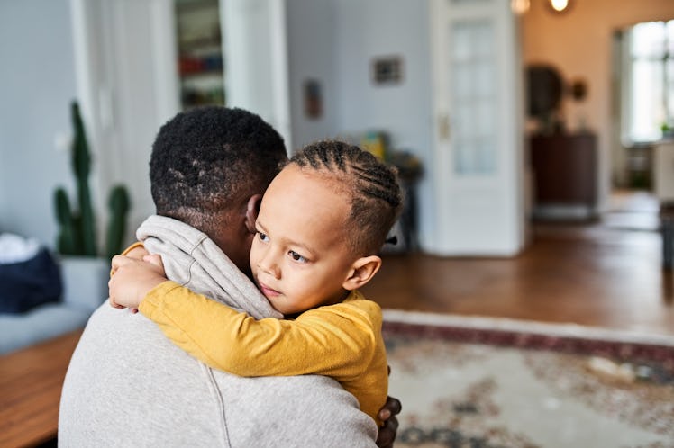 A Black child hugging their father at home.