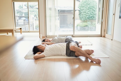 A man and woman on the floor on yoga mats, stretching with a lower body twist.