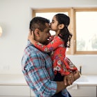 Young daughter kissing father on the head as he holds her