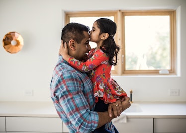 Young daughter kissing father on the head as he holds her
