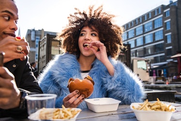 Young woman eating a burger during Mercury retrograde spring 2023, which will affect her zodiac sign...