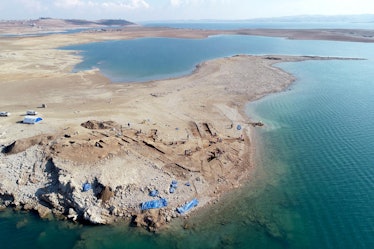 photo of a sandy peninsula with ruined brick building foundations jutting out into a lake of blue wa...