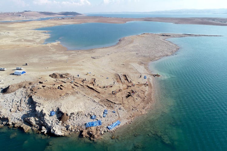 photo of a sandy peninsula with ruined brick building foundations jutting out into a lake of blue wa...