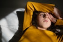 A sad preteen child lying in the dark on a bed, partially covering their face.