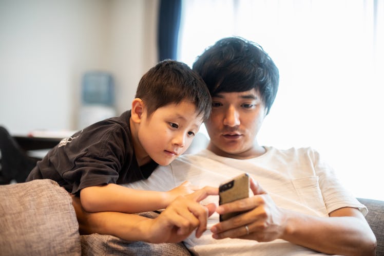 A dad and son on a couch watching TikToks on a phone.