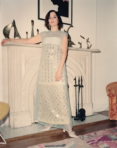 the actor Parker Posey poses against a fireplace in a sheer dress with shimmering pailletes
