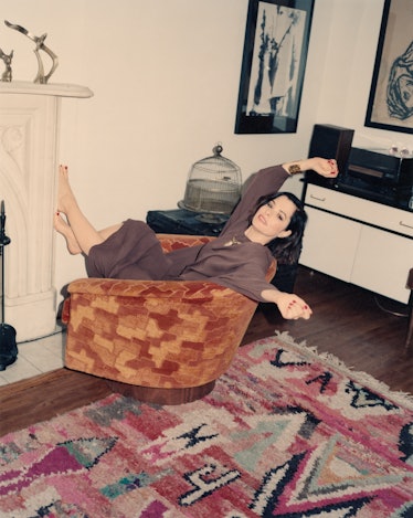 The actor Parker Posey reclining in a velvet armchair