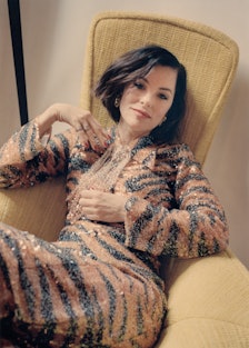 Parker Posey wearing a tiger print, sequined Gucci dress, lounges in a mid-century yellow chair
