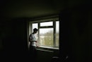 一个男人在一个黑暗的房间里，盯着窗外，抽着烟。