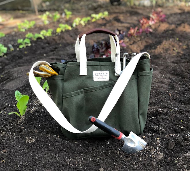 Mother's Day gifts for gardners: a nine-pocket tote bag sits in the soil with gardening tools nearby