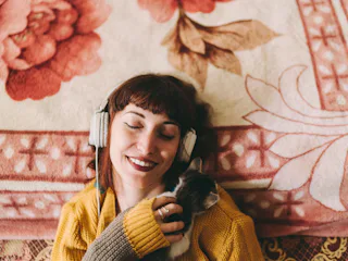 Young woman listening to a podcast and holding a cat before her zodiac sign has the best sleep ever.