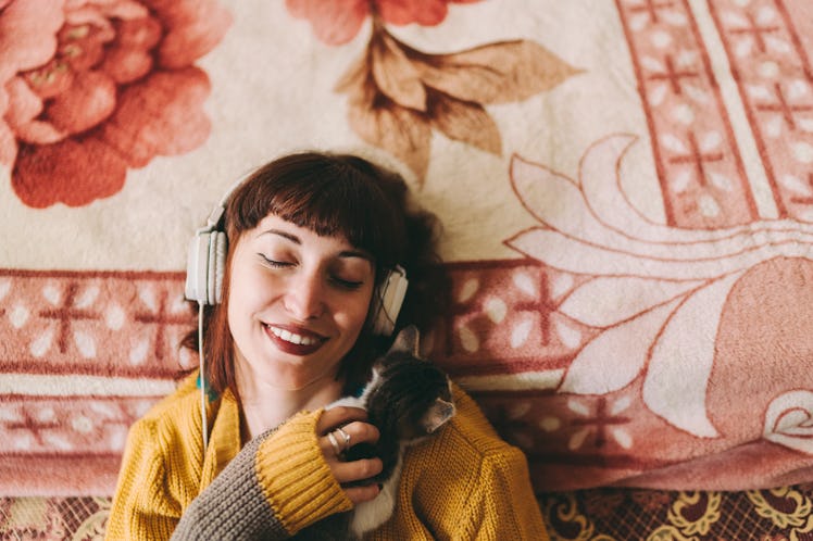 Young woman listening to a podcast and holding a cat before her zodiac sign has the best sleep ever.
