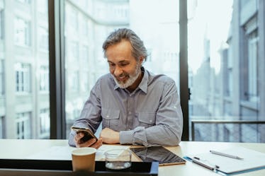 A man with grey hair sitting in an office, looking at his phone.