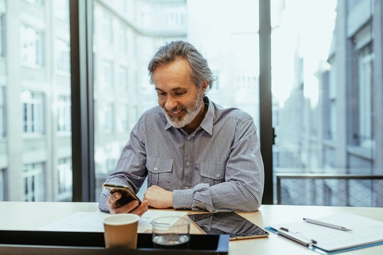 A man with grey hair sitting in an office, looking at his phone.