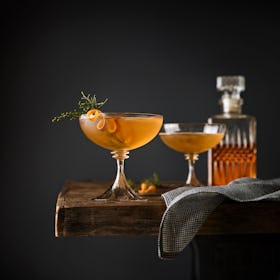 Two whiskey cocktails with citrus peels in coupe glasses set on bar 