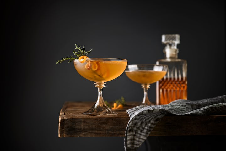 Two whiskey cocktails with citrus peels in coupe glasses set on bar