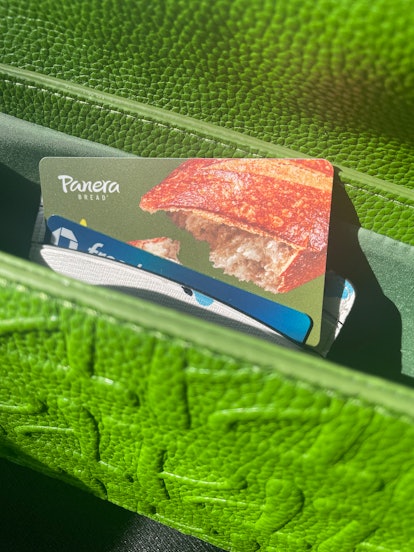 A Panera gift card sticking out of a wallet in a green purse