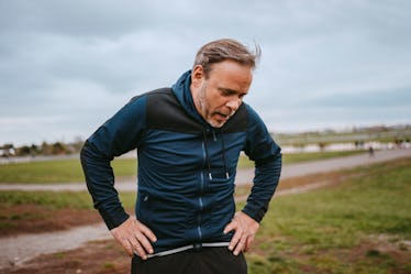 A tired man with hands on his hips, taking a break while on a run outdoors.