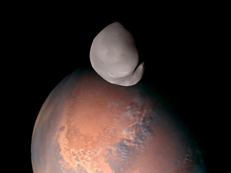 A lumpy gray moon hangs in the foreground, with the reddish-brown half-circle of Mars behind and bel...