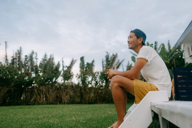 A happy man sitting on the step of his porch, overlooking nature.