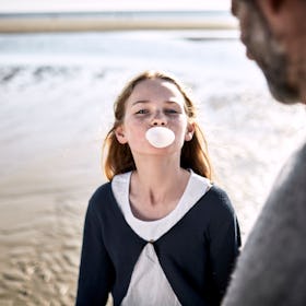 A daughter chews gum and blows a bubble on the beach as her dad watches.