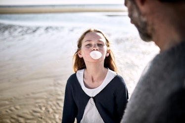 A daughter chews gum and blows a bubble on the beach as her dad watches.