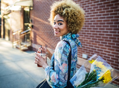 Young woman holding a coffee and carrying a bouquet after hearing the meaning of a Flower Moon.