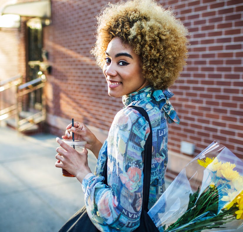 Young woman holding a coffee and carrying a bouquet after hearing the meaning of a Flower Moon.