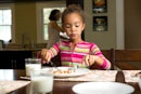 一个女孩坐在家里的餐桌上,用刀和叉吃她的食物。