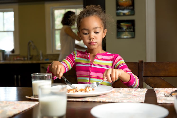 A girl sitting at the dinner table at home, eating her food with a knife and fork.