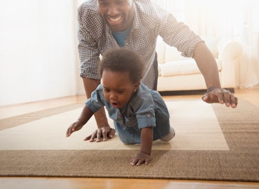 A dad and his daughter crawling on the floor together.