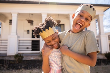 一对兄妹戴着自制的纸王冠，在他们的房子前拥抱欢笑。