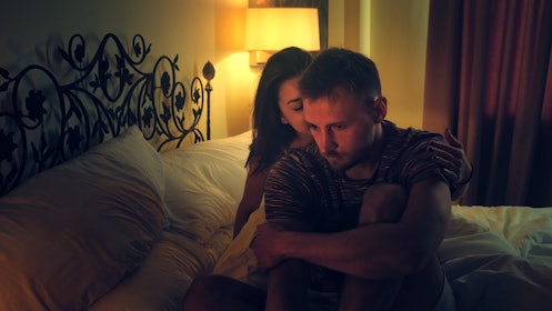 一个男人在做爱后坐在床上悲伤，而他的妻子安慰他。