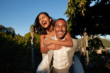 Beaming man giving happy bride a piggy back ride