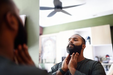 A man touching his beard while looking in a mirror.