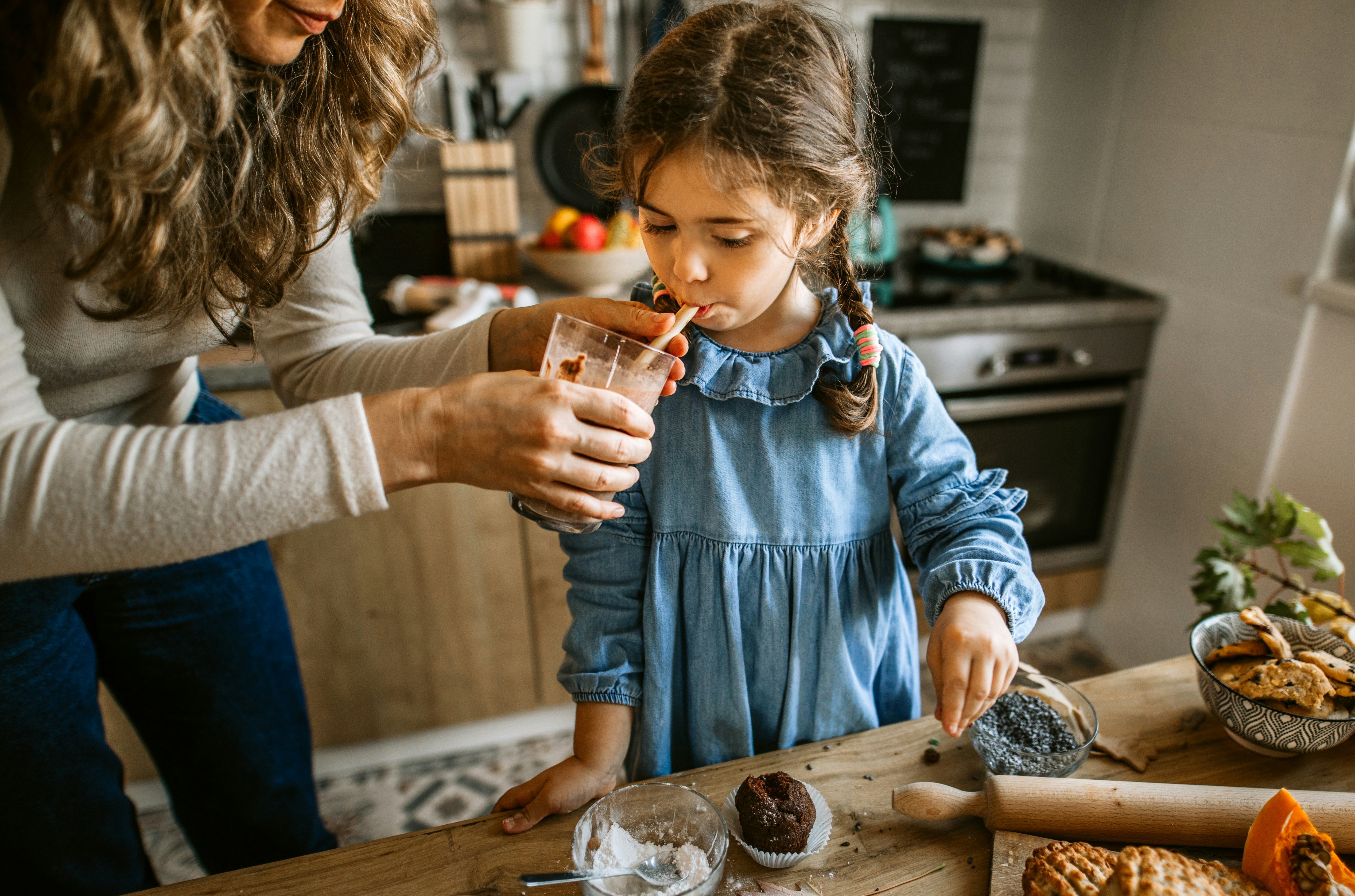 妈妈帮助她的女儿喝蛋白奶昔对孩子在他们的厨房。