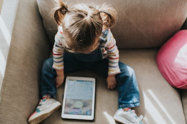 A young girl on the couch looking at a tablet screen.