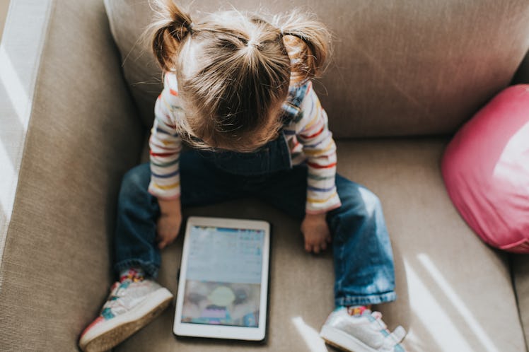 A young girl on the couch looking at a tablet screen.
