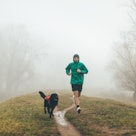 A man going for a jog in the rain with his dog.