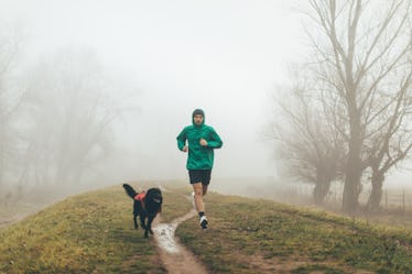 A man going for a jog in the rain with his dog.