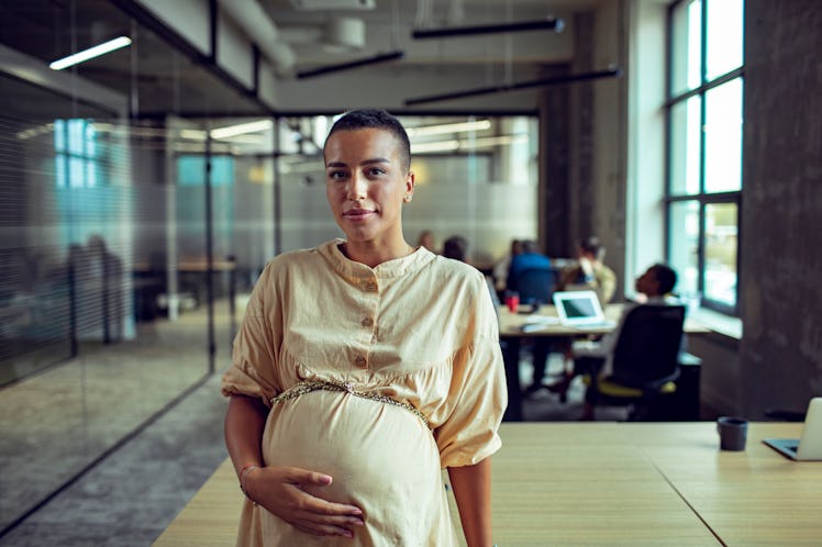Pregnant woman smiling and touching her belly in workplace