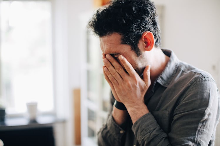 A man at work in a home office, burying his head in his hands.