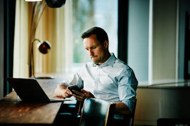 Middle aged man at work looking at phone as he thinks about a big decision