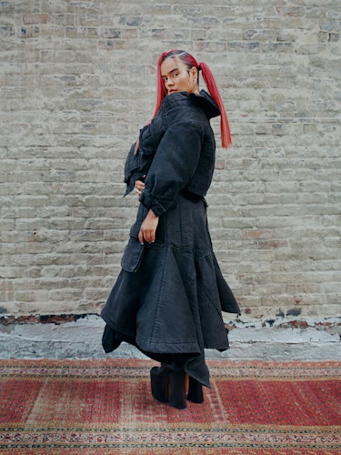 Karol G wears a dark denim jacket, dark denim skirt, earrings and platform boots.