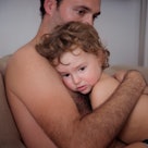 An upset dad hugging his child while sitting on a couch.