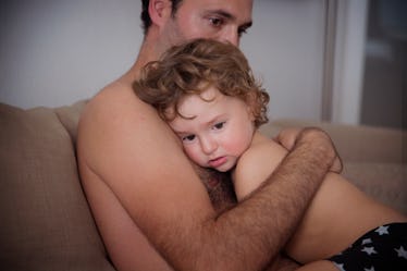 An upset dad hugging his child while sitting on a couch.