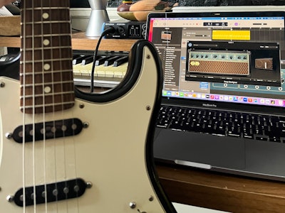 A guitar in front of a MacBook Pro with GarageBand open
