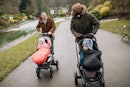 两个爸爸推着婴儿车走在公园的小路上。