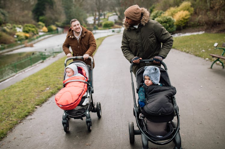 Two dads pushing their babies in strollers down a path in a park.